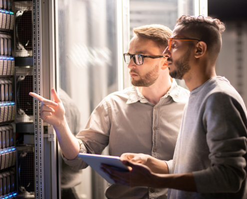 Two specialists standing at server and using tablet while managing network server together in data center