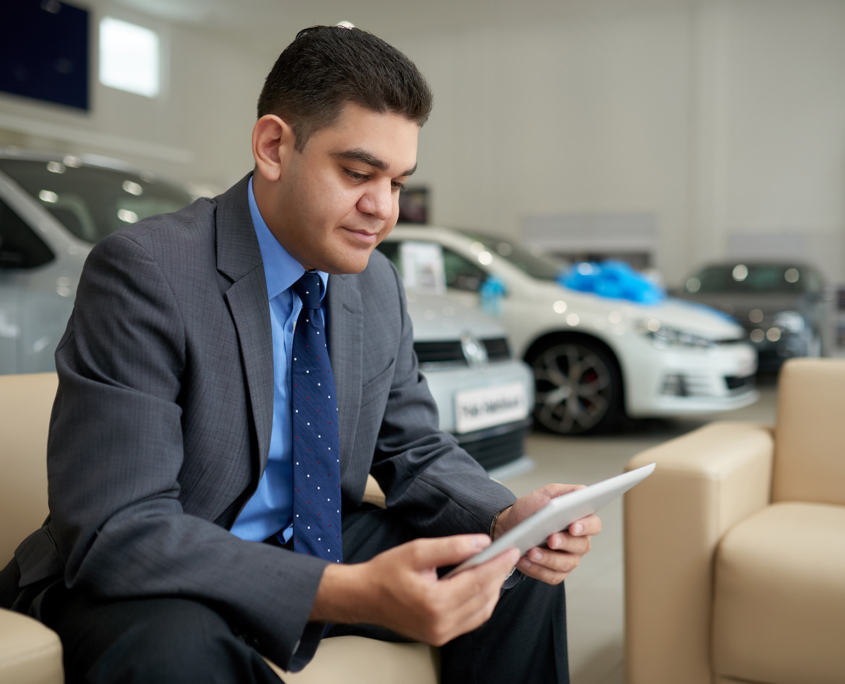 Smiling car dealer reading information on digital tablet